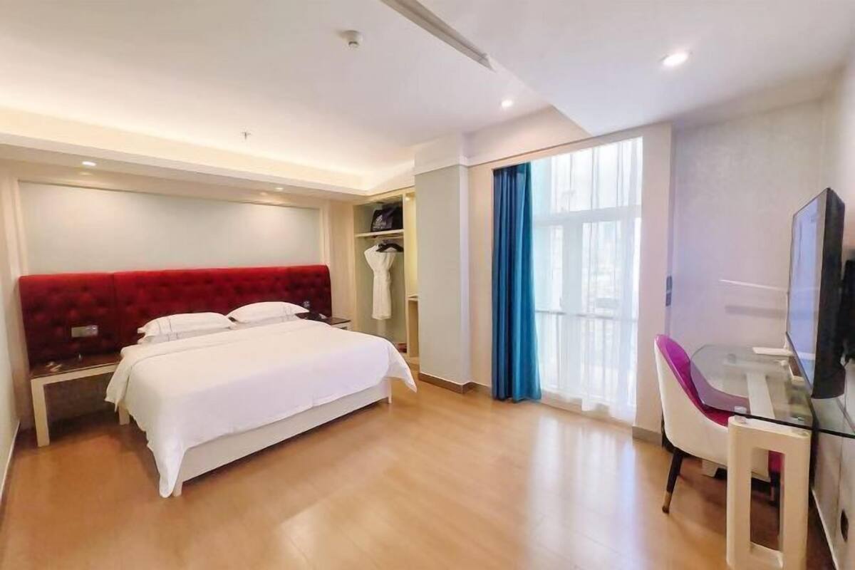 Une chambre d’hôtel moderne équipée d’un lit, d’un bureau, d’une chaise, d’une télévision et d’une fenêtre avec des rideaux.