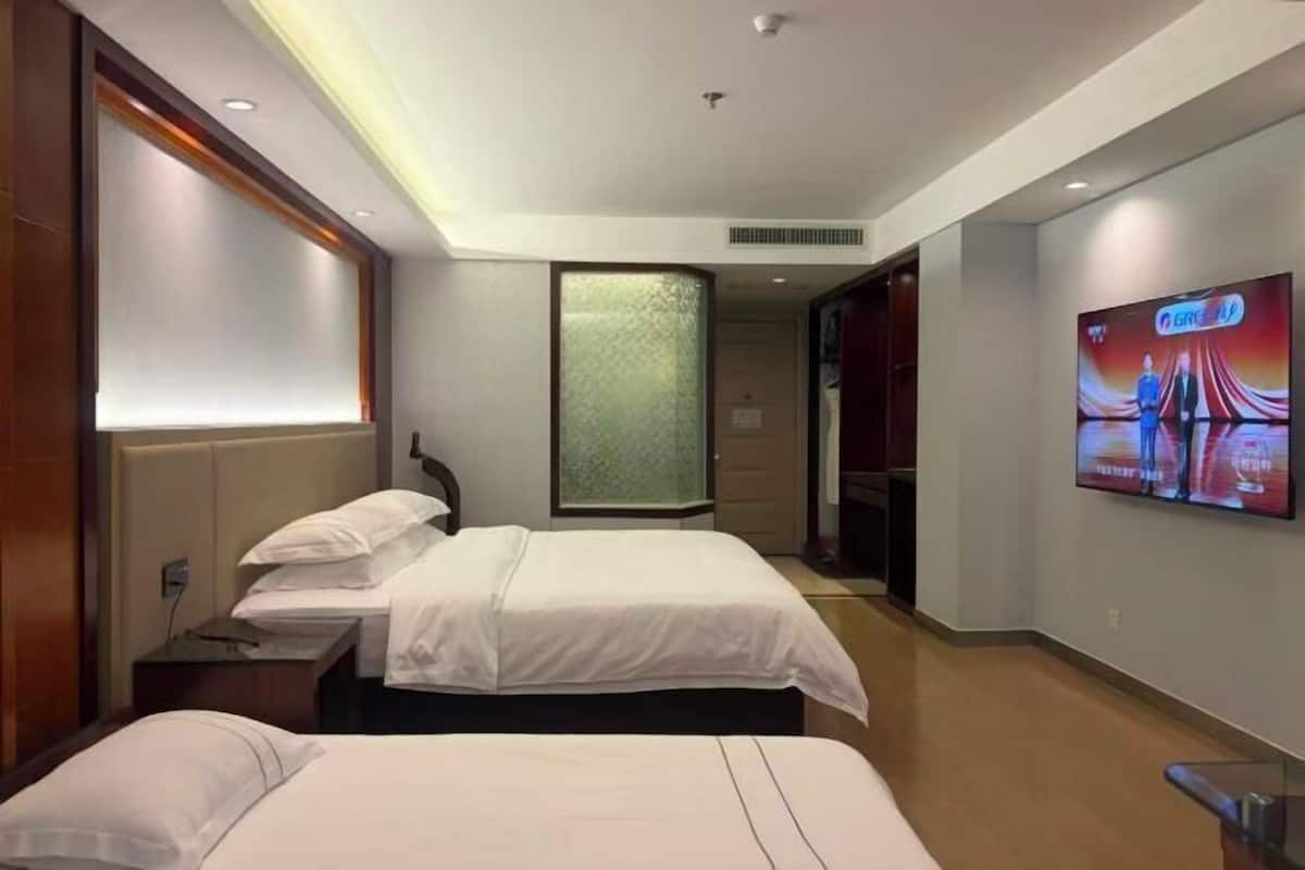 Une chambre d’hôtel avec deux lits, un téléviseur fixé au mur et une grande fenêtre.