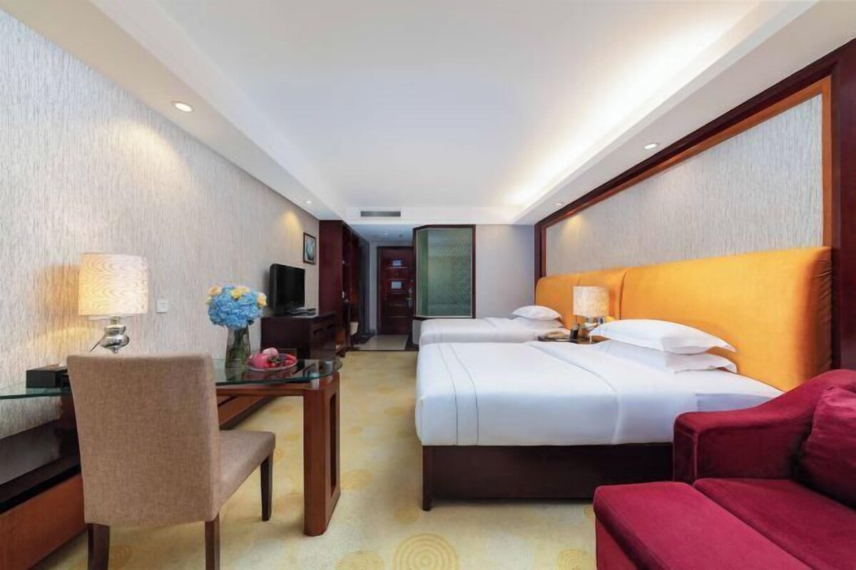 Une chambre d’hôtel avec un bureau, deux lits, un canapé rouge et une télévision.