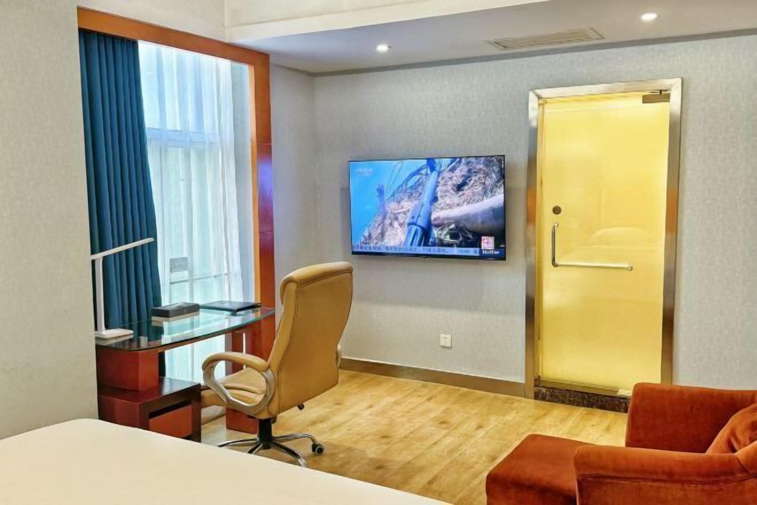 A hotel room with a bed, a desk with a chair, a television mounted on the wall, and a door.