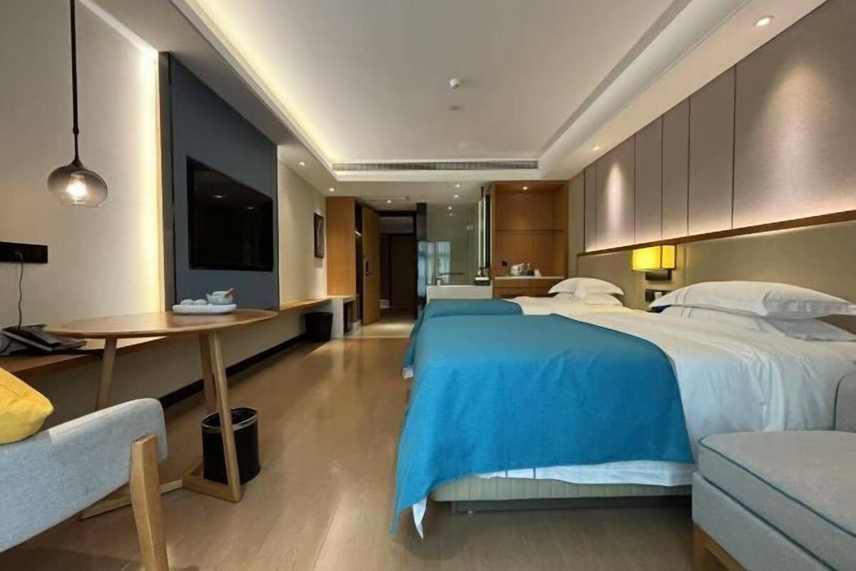 Une chambre d’hôtel avec un lit, un bureau, une chaise et une petite table. Il y a un miroir au mur et une lampe sur le bureau.
