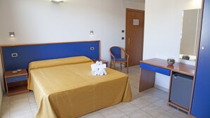 Une chambre d’hôtel équipée d’un lit, d’un bureau, d’une chaise, d’un petit réfrigérateur et d’un miroir.