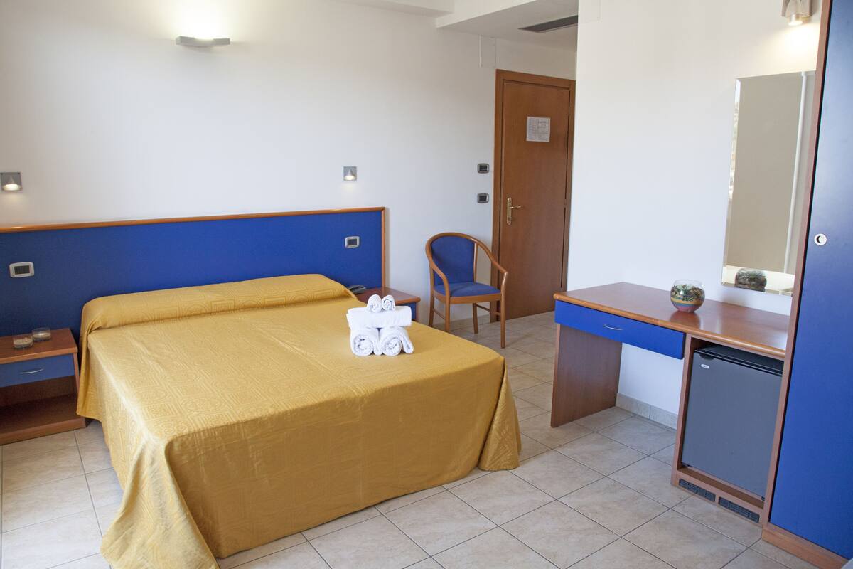 Ein Hotelzimmer mit Bett, Schreibtisch, Stuhl, kleinem Kühlschrank und Spiegel.