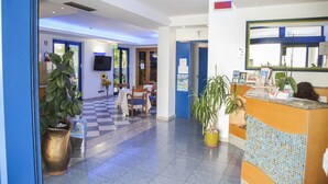 Un hall d’hôtel avec un sol à carreaux, un comptoir d’accueil et un espace détente avec des tables et des chaises.