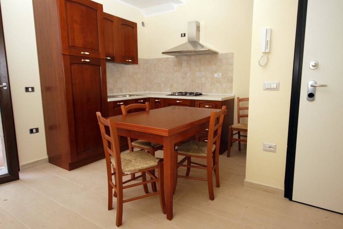 A compact kitchen with wooden cabinets, a gas stove, and a dining table with chairs.