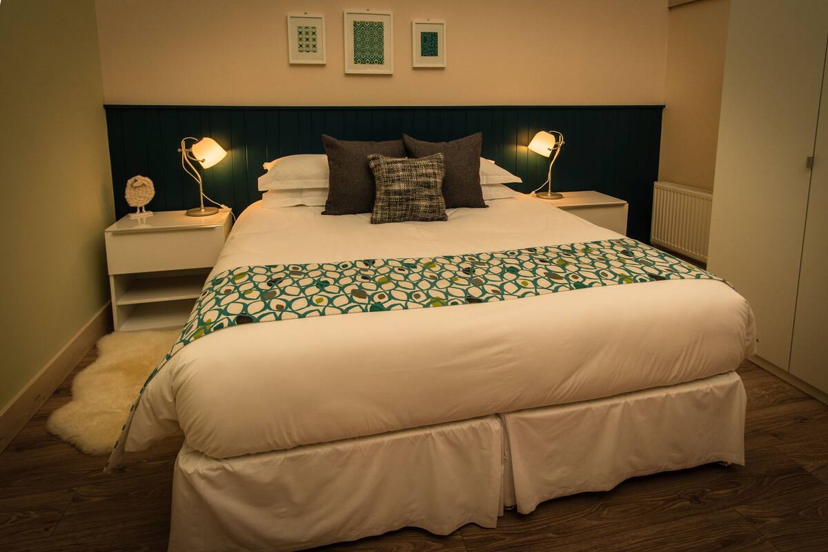 A neatly made bed with a patterned bedspread, two bedside lamps, and a wall-mounted shelf.