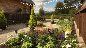 A wooden cabin with a gravel garden, surrounded by trees and mountains. - Faebuie Cottages (Inverness)