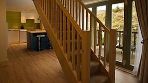A modern kitchen with wooden flooring, a wooden staircase, and a view of the outdoors through large sliding glass doors. - Faebuie Cottages (Inverness)
