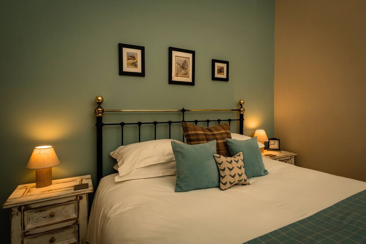 A neatly made bed with a metal headboard, two bedside tables with lamps, and three framed pictures on the wall.