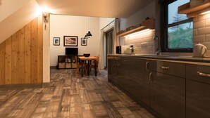 A kitchen with wooden flooring, a dining area with a table and chairs, and a window with a view of greenery. - Faebuie Cottages (Inverness)