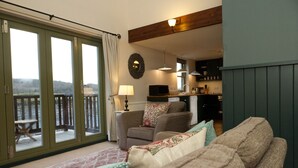 A cozy living room with a sofa, a chair, and a view through a sliding glass door to an outdoor deck. - Faebuie Cottages (Inverness)