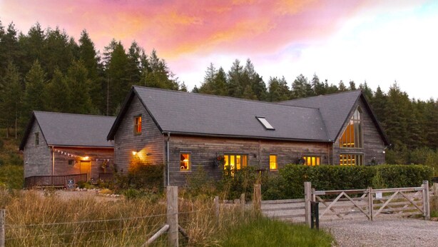 A rustic wooden cabin with a sloped roof, large windows, and a wooden fence in front. - Faebuie Cottages (Inverness)