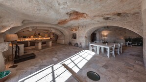 A spacious underground dining area with stone arches, a central table, and a bar area with stools. - Masseria Torre Abate Risi (Fasano)