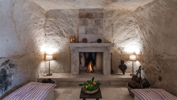 A stone-walled room with a fireplace, two lamps, and a small table with a basket of flowers. - Masseria Torre Abate Risi (Fasano)