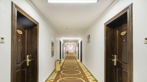 A hotel hallway with dark wooden doors, a patterned carpet, and a long corridor leading to a bright end. - Nanning Shenxianju Hotel (Jiangnan Passenger Transport Terminal) (Nanning)