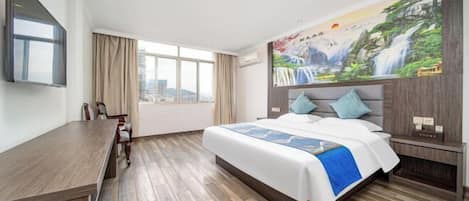 A hotel room with a large bed, a desk, a chair, a TV, and a city view through the window.
