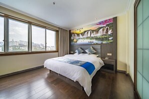 A modern hotel room with a large bed, a city view, and a mural of waterfalls on the wall.