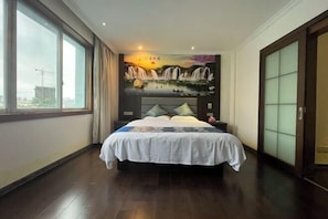 A bedroom with a large bed, a mural on the wall, a view through the window, and a sliding door.