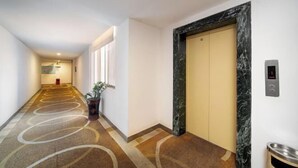 A hotel hallway with a marble elevator, a potted plant, and a metal trash bin. - Nanning Shenxianju Hotel (Jiangnan Passenger Transport Terminal) (Nanning)
