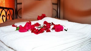 Una cama bien hecha con una toalla blanca y flores rojas dispersas.