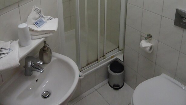 A bathroom with a shower, sink, toilet, and a trash bin. - CityHotel Magdeburg (Magdeburg)