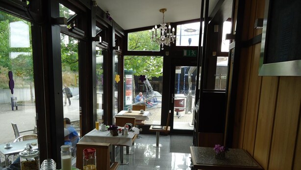 An indoor dining area with tables and chairs, a chandelier, and large windows. - CityHotel Magdeburg (Magdeburg)