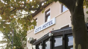 A city hotel with a sign above the entrance, a sculpture in front, and a person walking by. - CityHotel Magdeburg (Magdeburg)