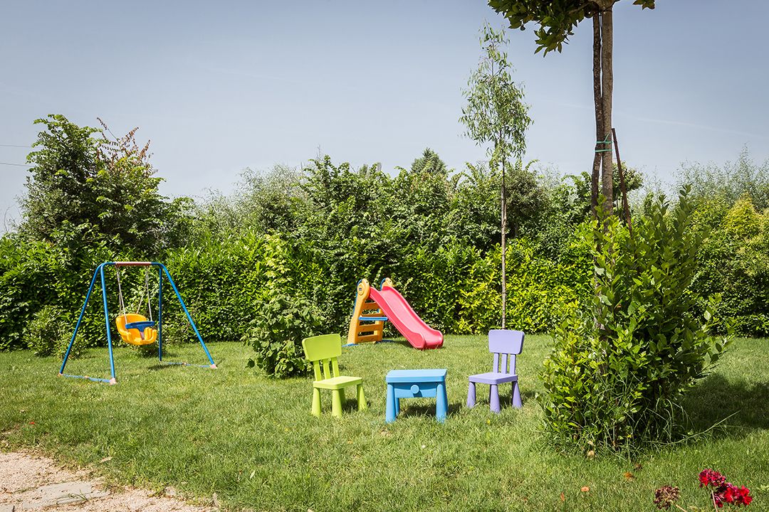 Un espace extérieur verdoyant avec une balançoire, deux toboggans et trois petites tables.