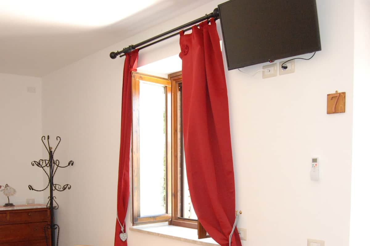 Un dormitorio con cama, un armario de madera, un televisor montado en la pared y una ventana con cortinas rojas.