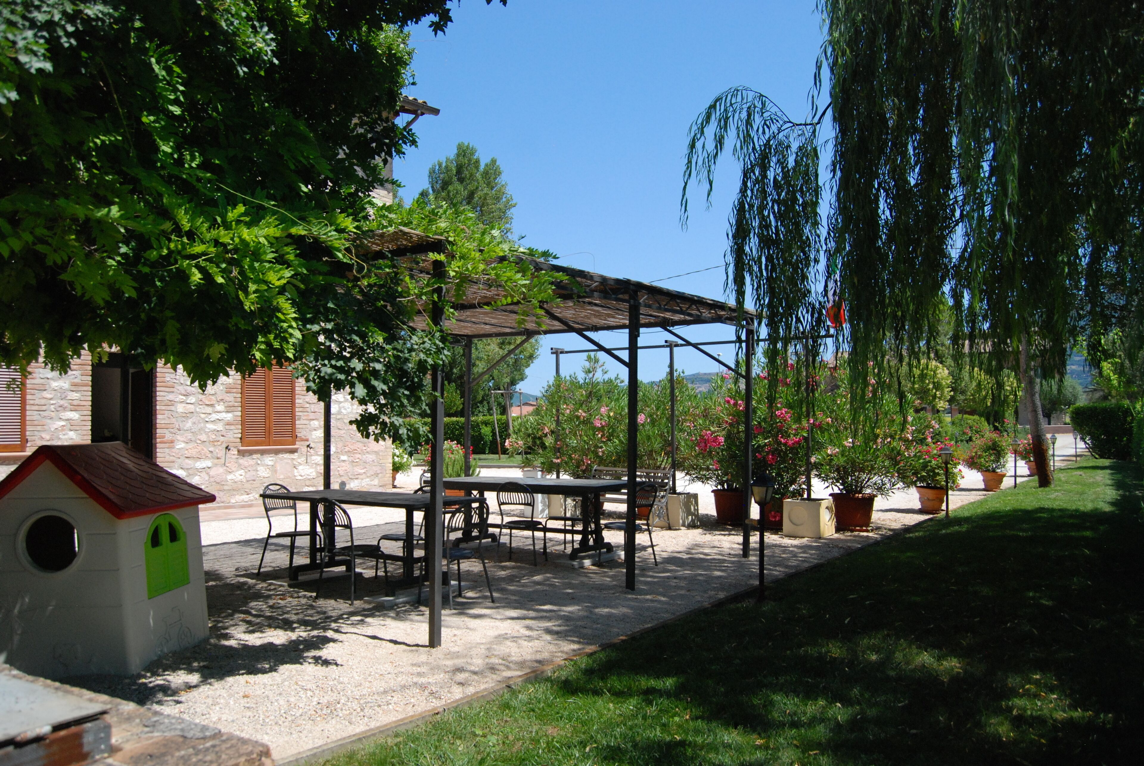 Ein Terrassenbereich im Freien mit Tisch und Stühlen, einem kleinen Spielhäuschen und Kübelpflanzen.