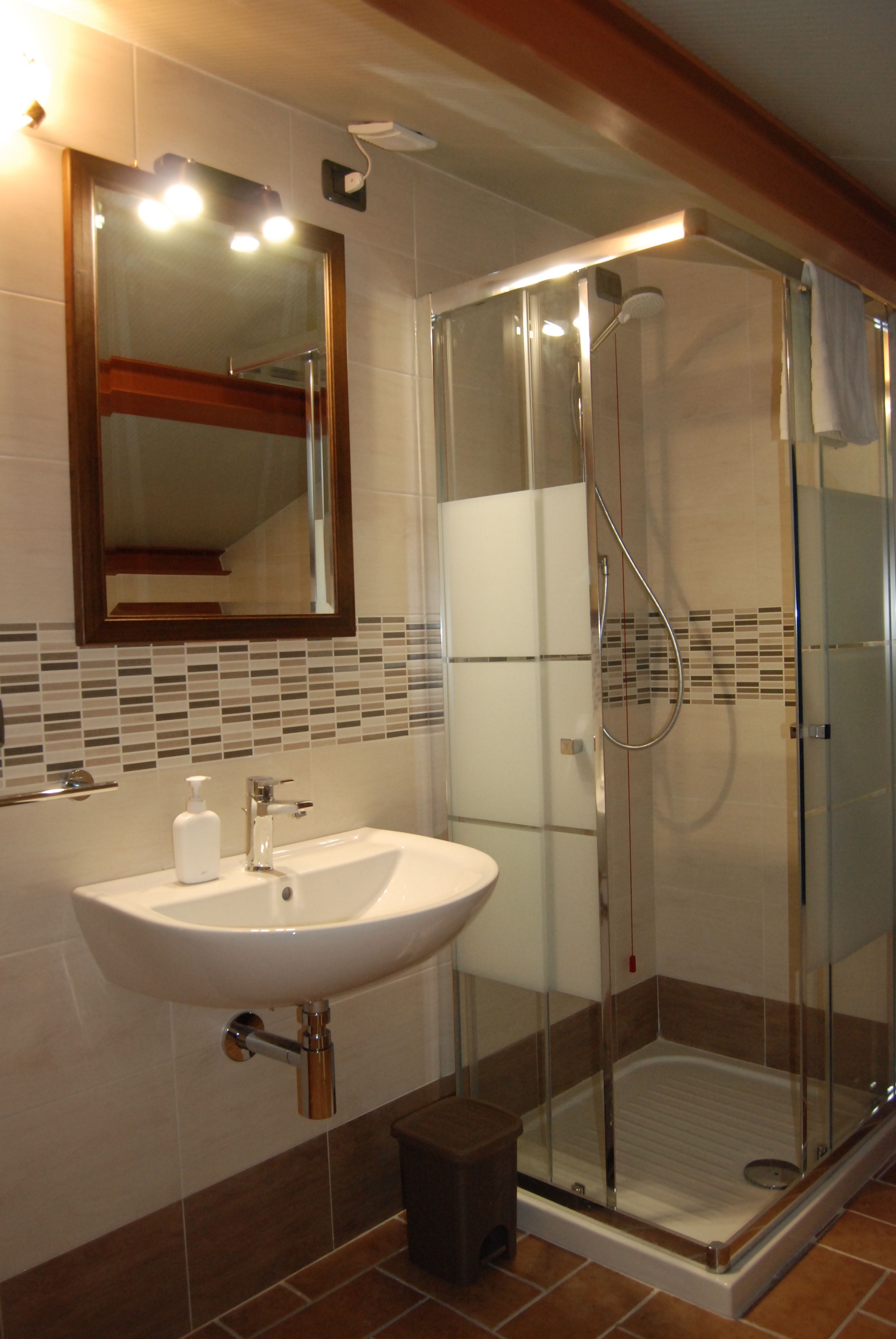 A bathroom with a glass-enclosed shower, a sink with a mirror above it, and a trash bin.