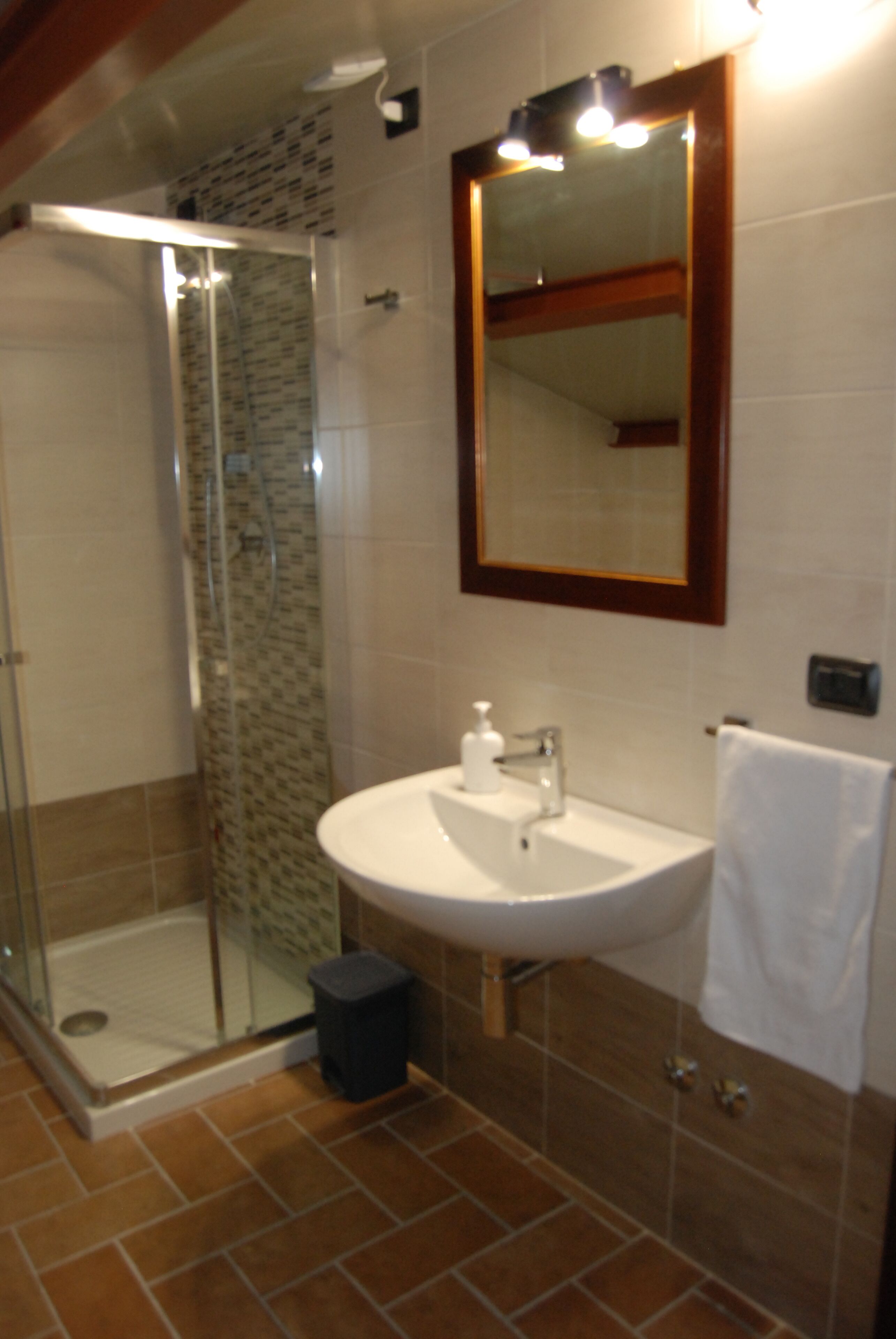 A bathroom with a glass-enclosed shower, a sink with a mirror, and a white towel hanging on the wall.