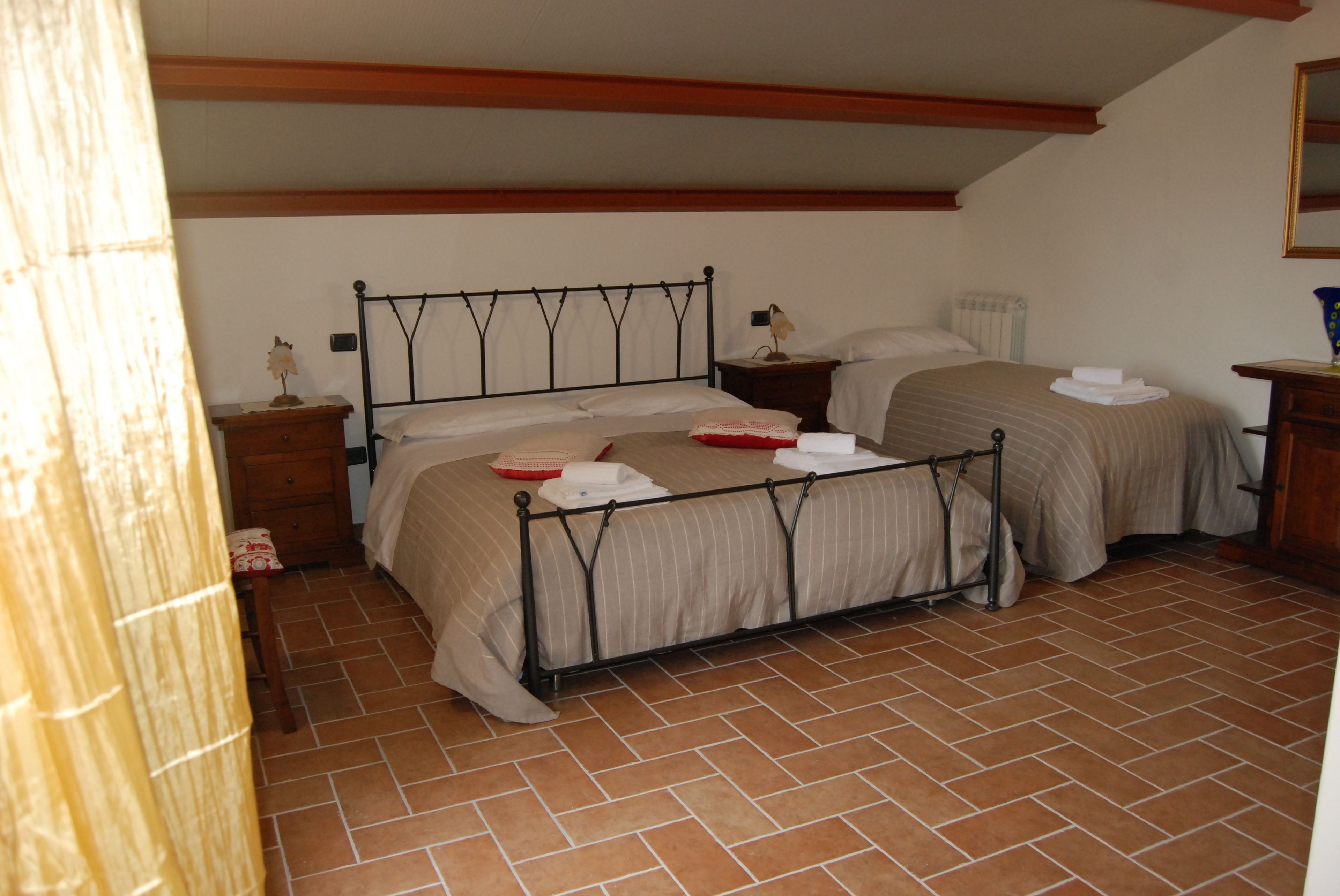 A bedroom with two beds, wooden headboards, a tiled floor, and a nightstand with a lamp.