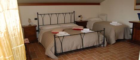 A bedroom with two beds, wooden headboards, a tiled floor, and a nightstand with a lamp.