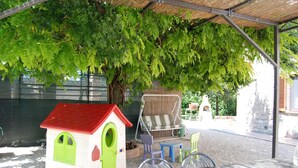 Un espace extérieur abrité comprenant une cabane de jeux, des sièges et un arbre qui offre de l’ombre.