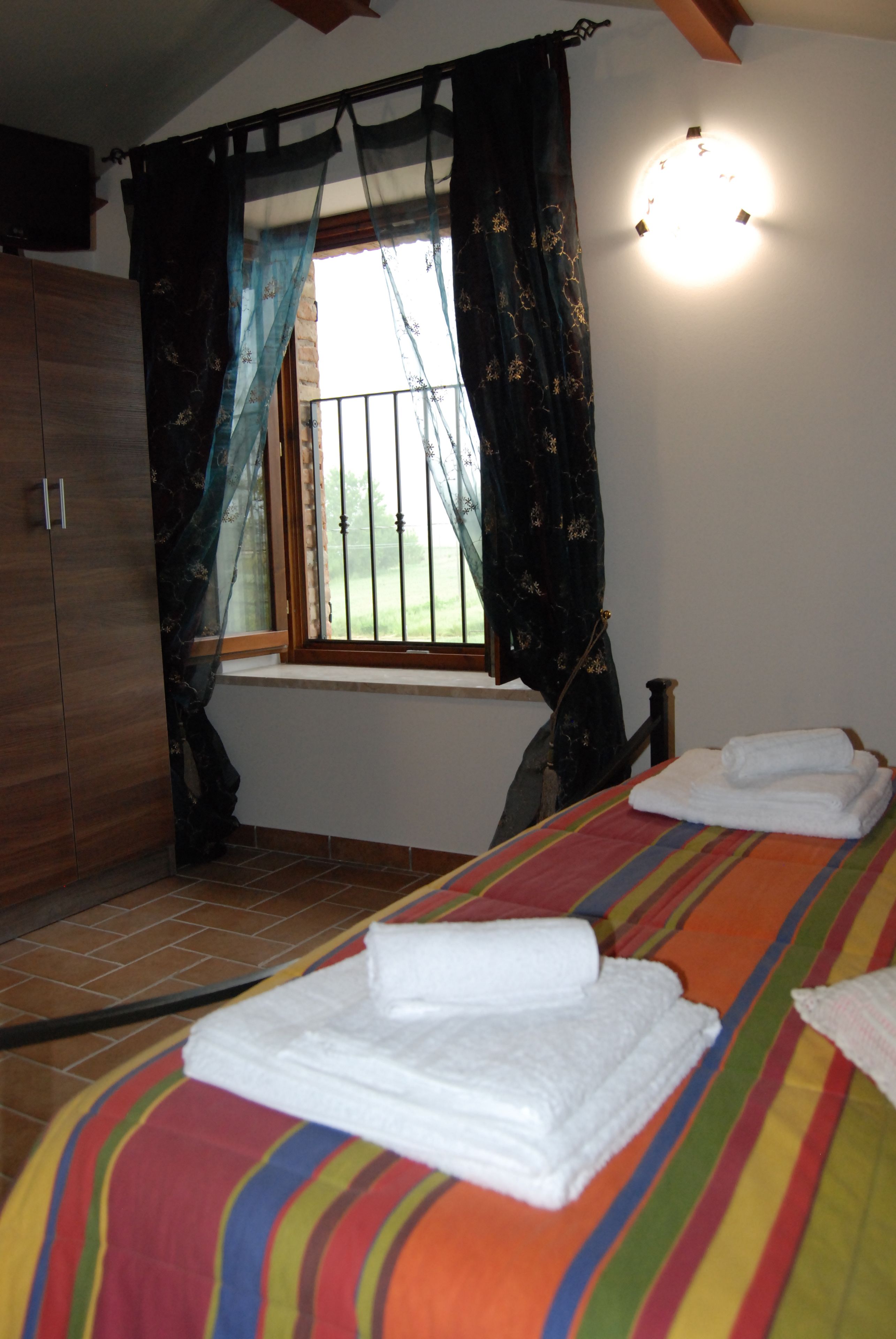 A bedroom with a bed, a window with curtains, a bedside table, and a wall-mounted light fixture.
