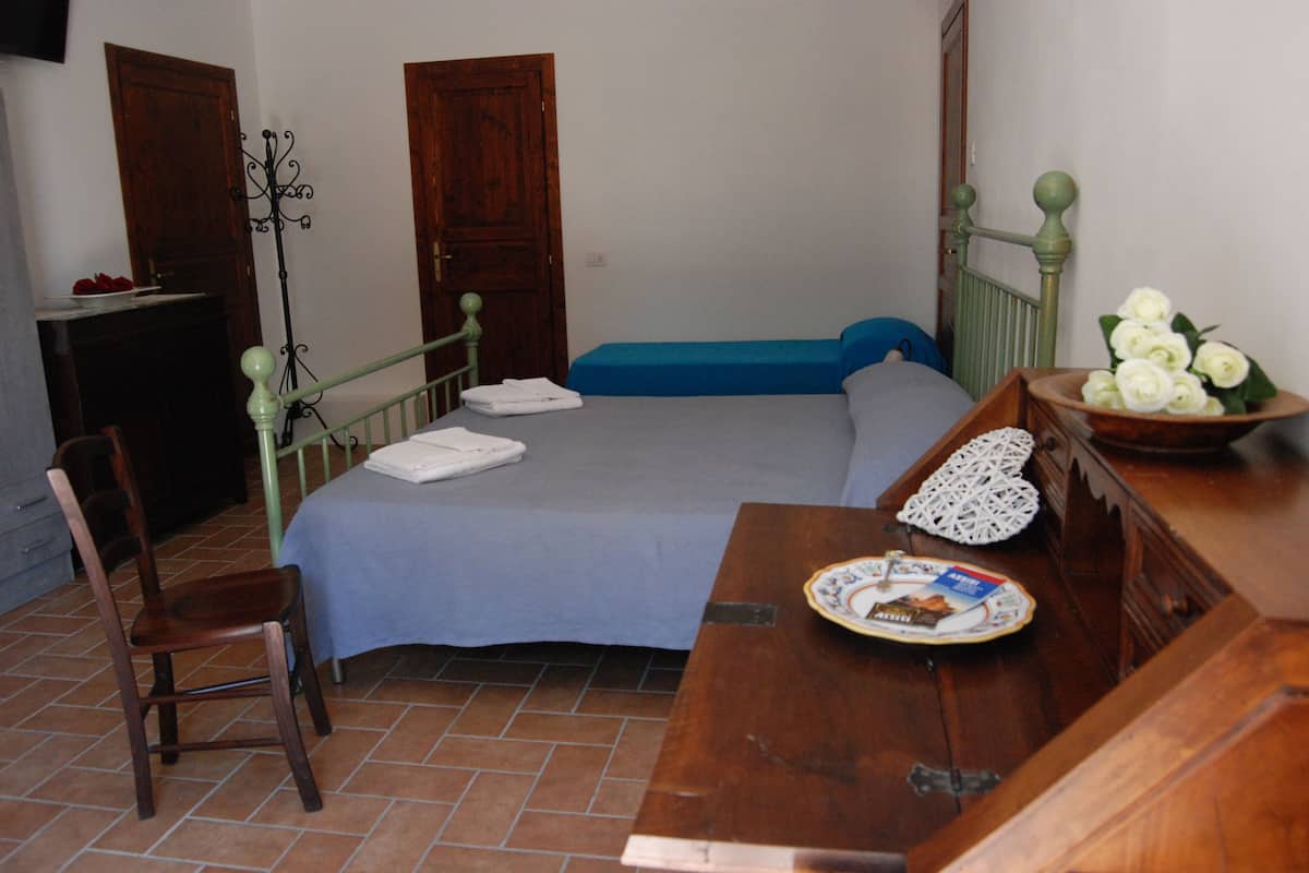 Un dormitorio con una cama, un aparador de madera, una silla y una mesa con un plato y un florero.
