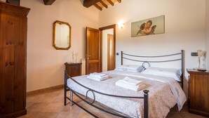 Une chambre à coucher avec un lit, une armoire en bois, un miroir et un tableau accroché au mur.