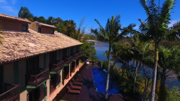 A hotel with a tiled roof, a pool, and palm trees. - Engenho da Lagoa Pousada (Garopaba)