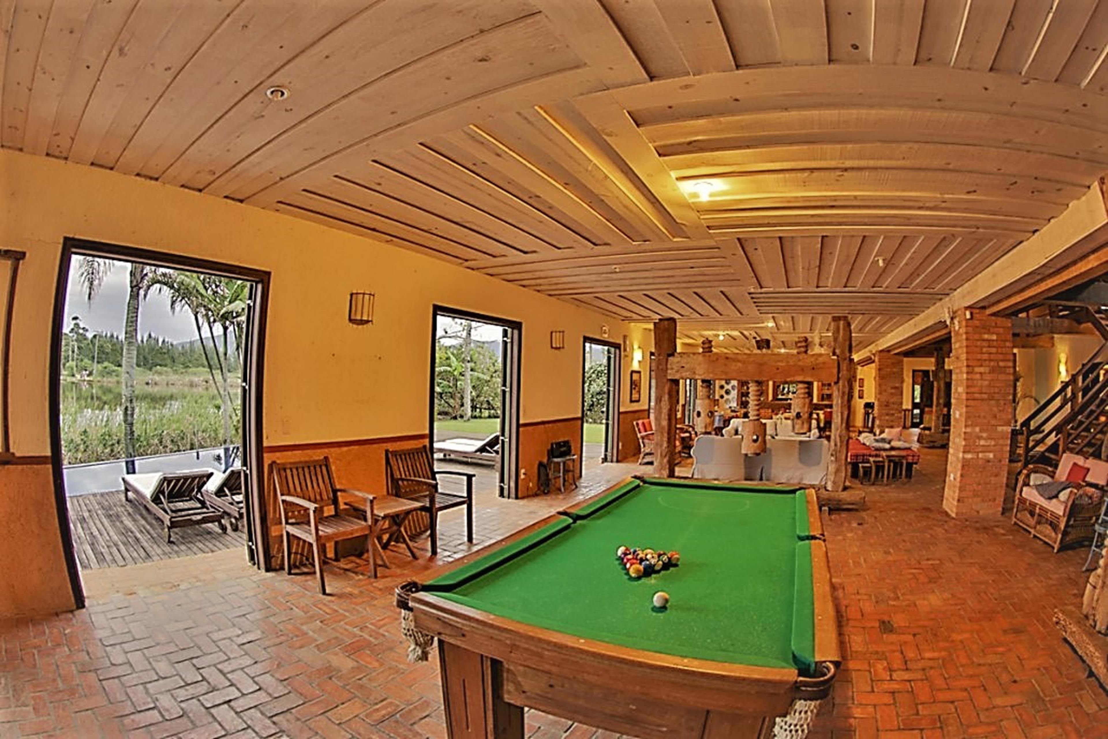 Zona de piscina con mesa de billar, sillas y vistas al exterior.