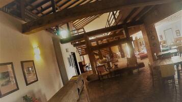 A spacious interior with a high ceiling, wooden beams, and a dining area with tables and chairs.