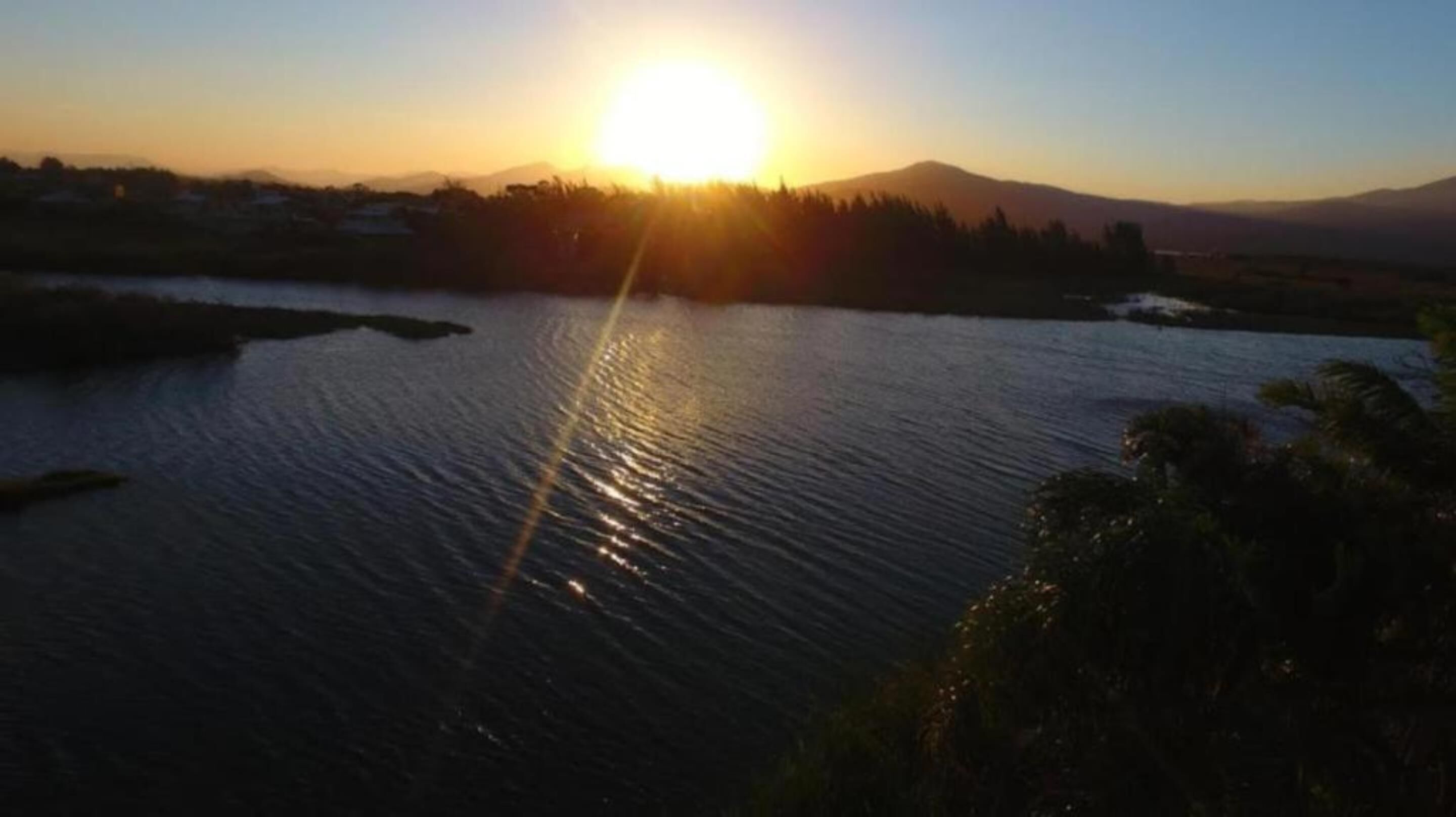 Un atardecer sobre un cuerpo de agua tranquilo, con una cadena montañosa distante.