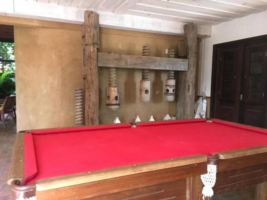 Una mesa de billar con superficie de fieltro rojo, estructura de madera y detalles decorativos en la pared de fondo.