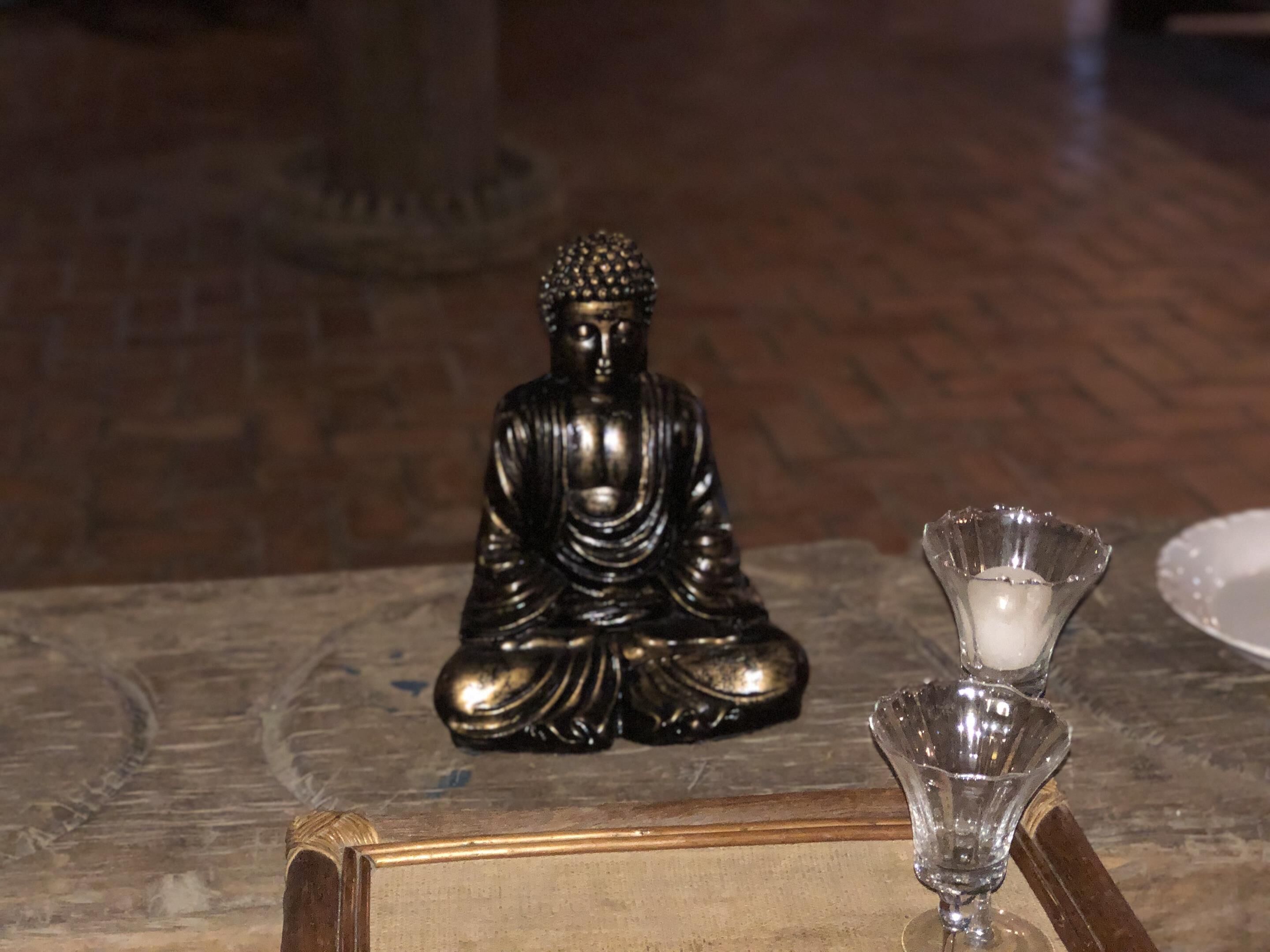 A Buddha statue on a marble table with a candle holder and a plate.