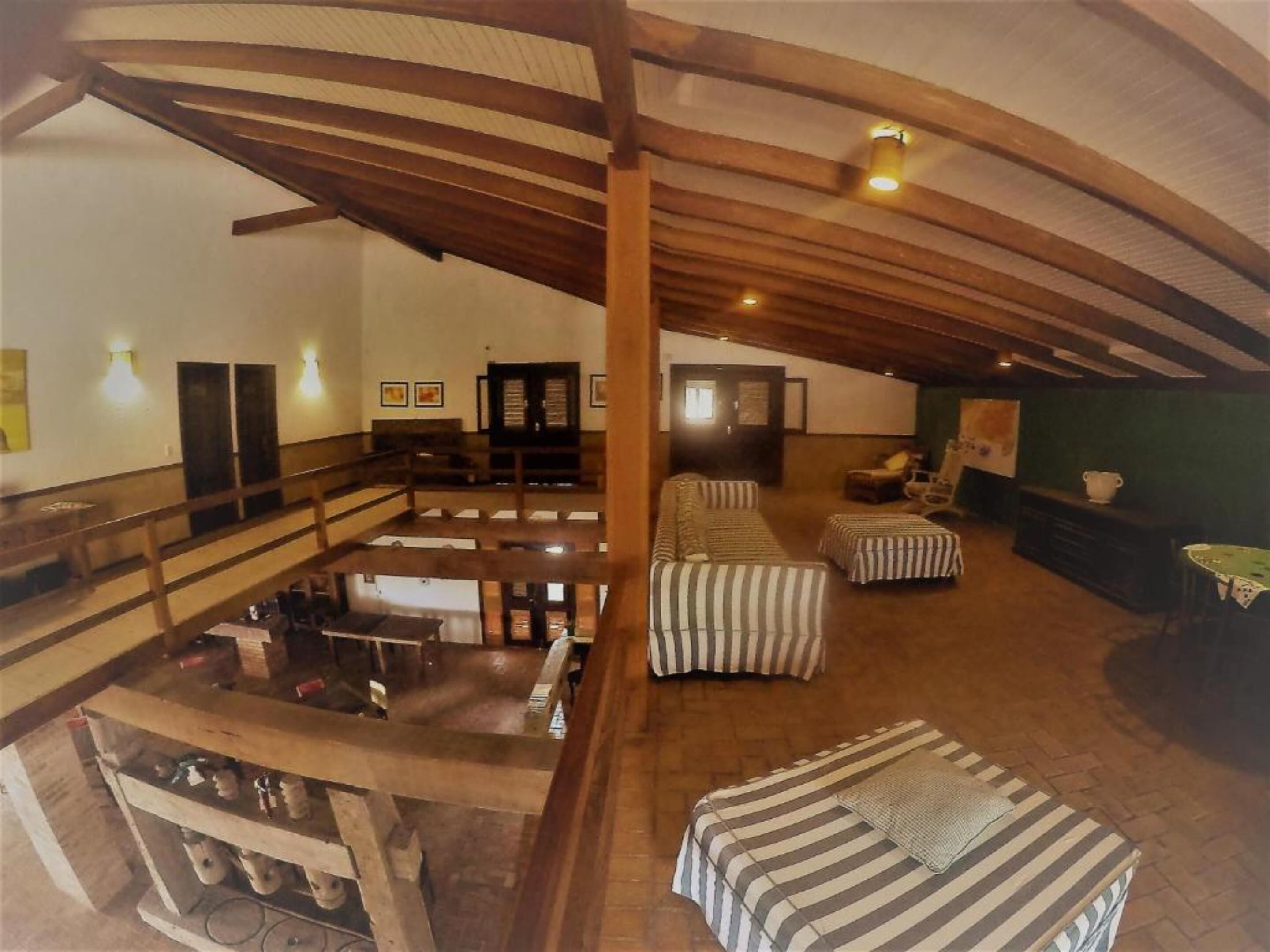 A spacious attic room with wooden beams, a loft bed, a sofa, and a table.