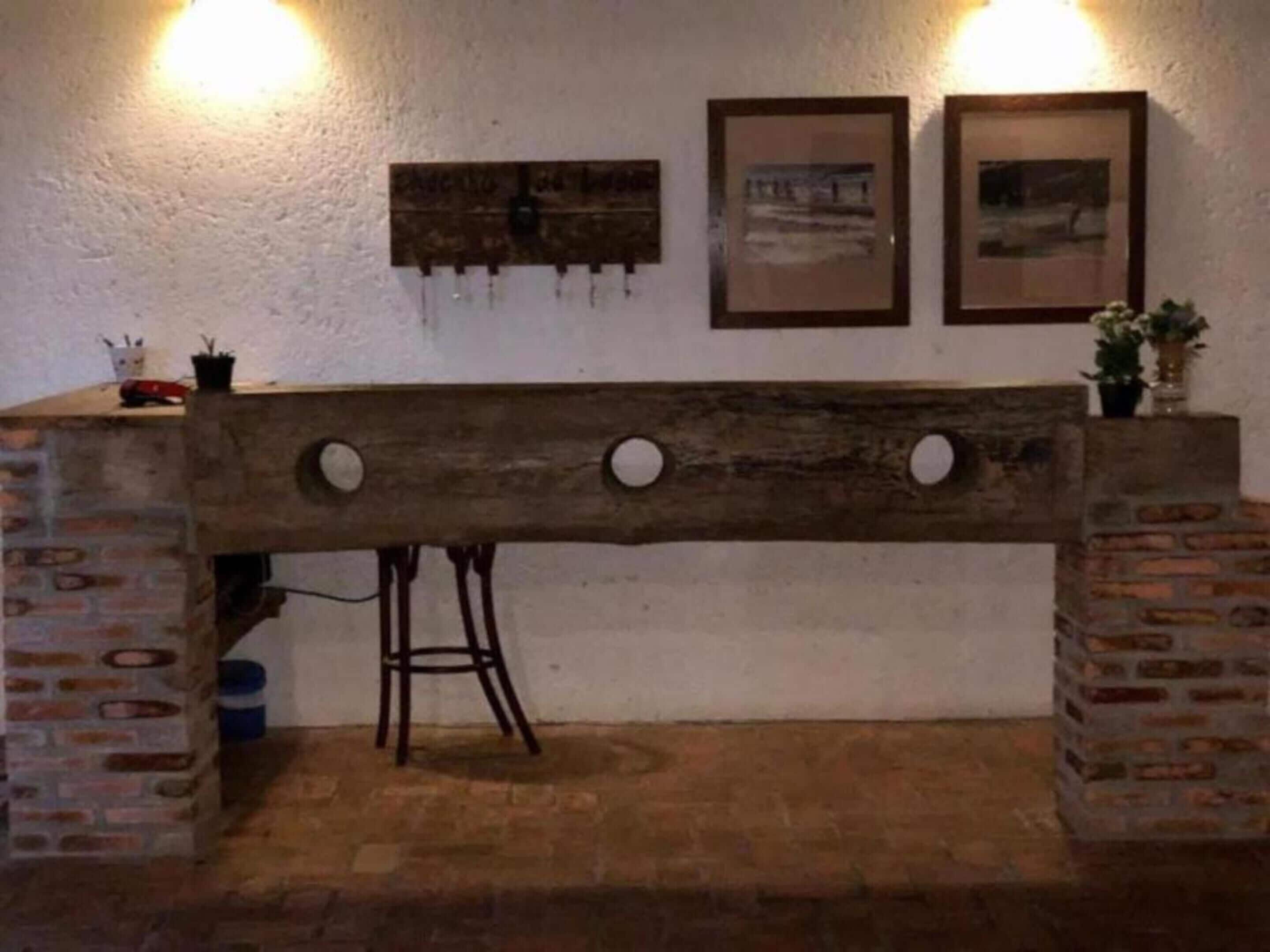 Een rustieke houten bank met ronde uitsparingen, geplaatst tegen een witte muur met twee ingelijste foto’s en twee wandlampen.