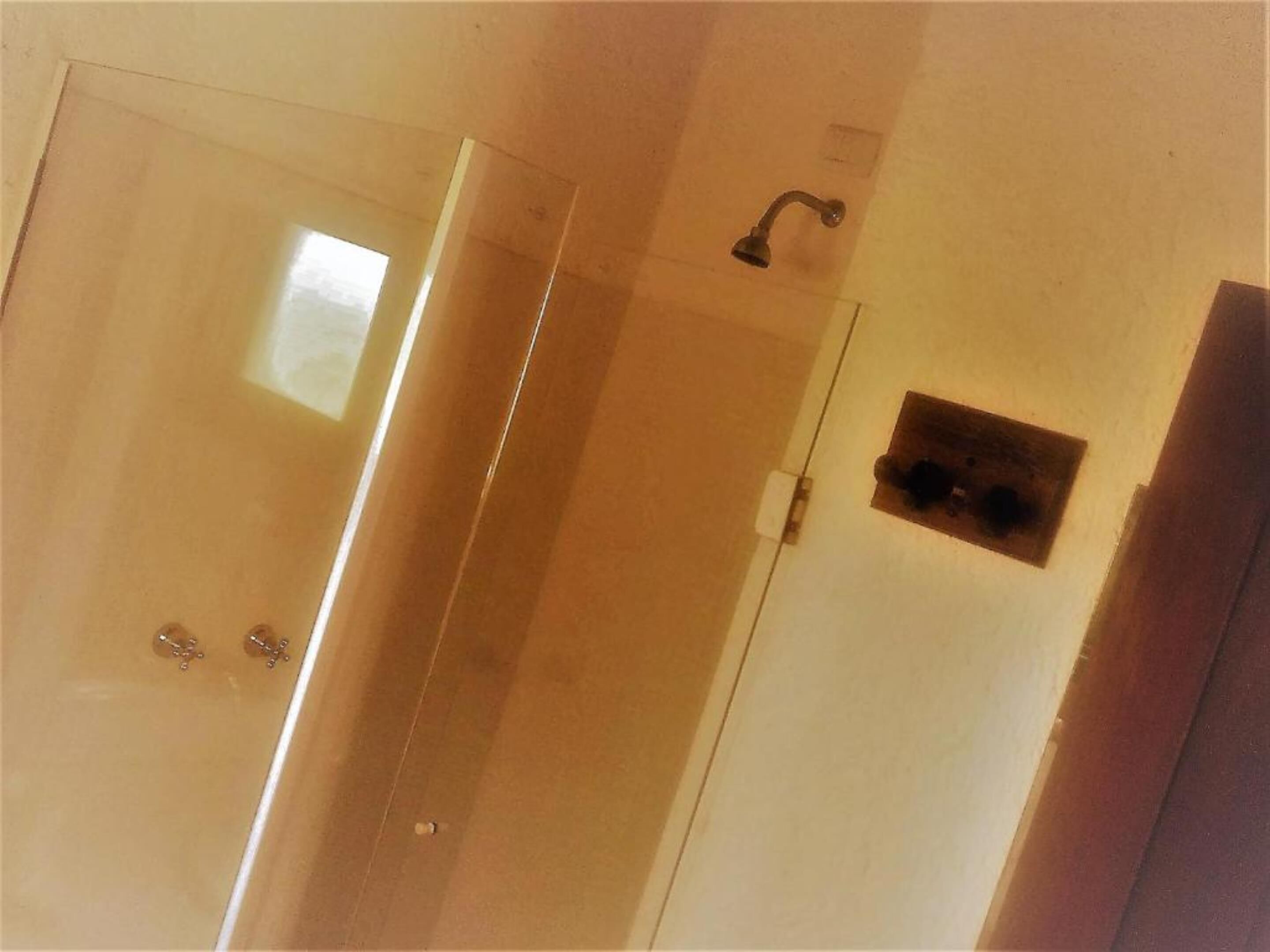 A bathroom with a glass shower enclosure, a white door, and a small window.