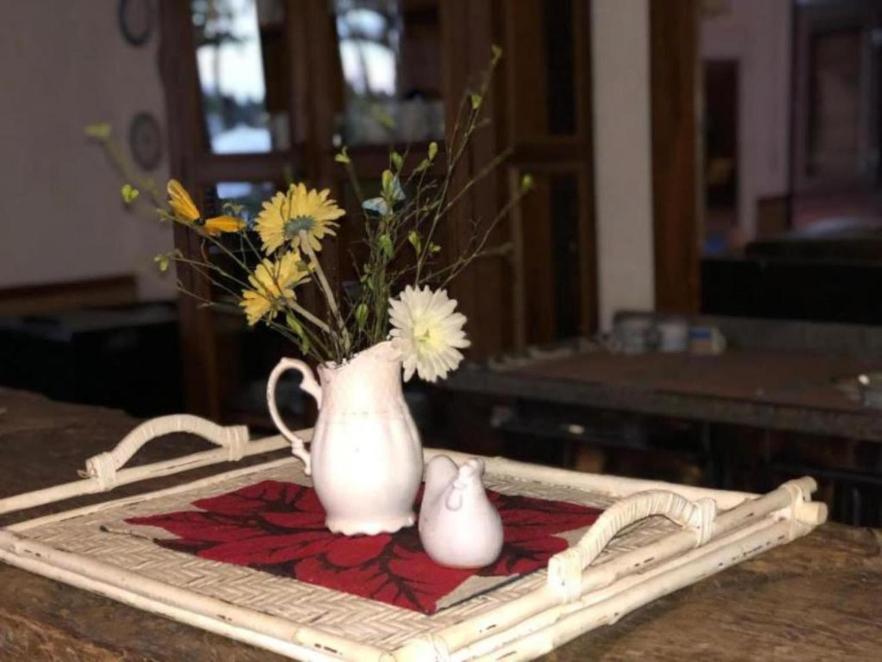 A white ceramic pitcher with flowers on a woven tray with a red leaf pattern.