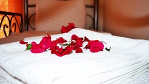 A neatly made bed with a white towel and scattered red flowers.