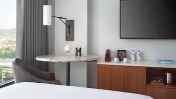 Une chambre d’hôtel comprenant un lit, une table ronde avec un vase, une lampe, un téléviseur à écran plat et un minibar.